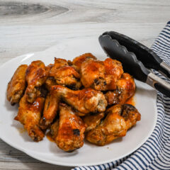 Hot honey wings on a serving plate with tongs.
