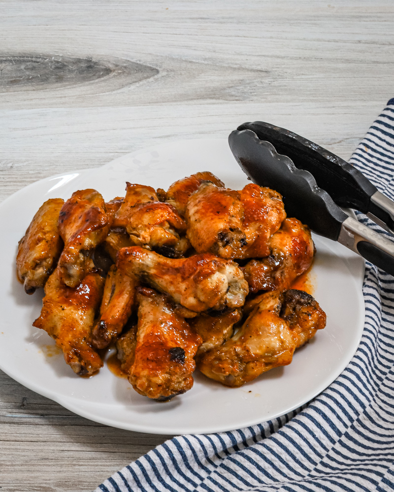 Hot honey wings on a serving plate with tongs.