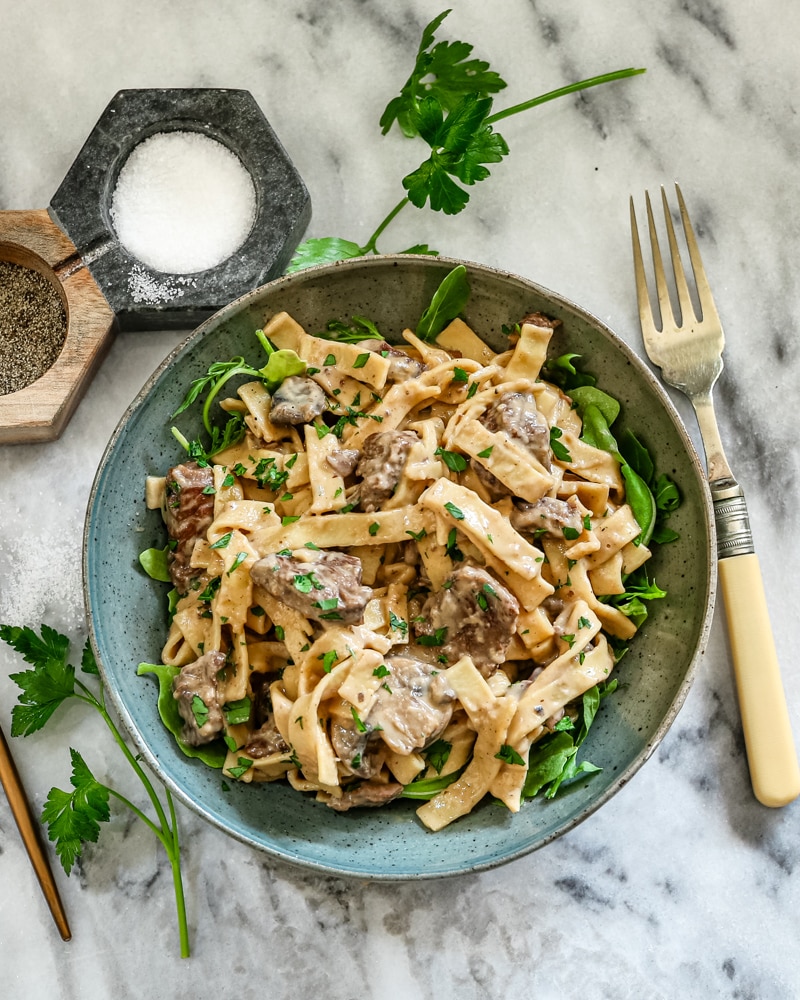 A bowl of Instant Pot beef stroganoff with parsley and arugula.
