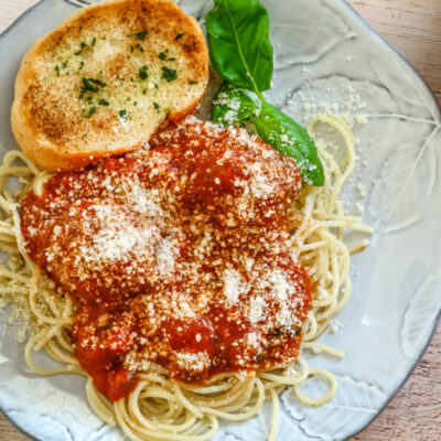 Homemade meatballs on a plate with spaghetti, garlic bread, and marinara sauce, sprinkled with Parmesan cheese.