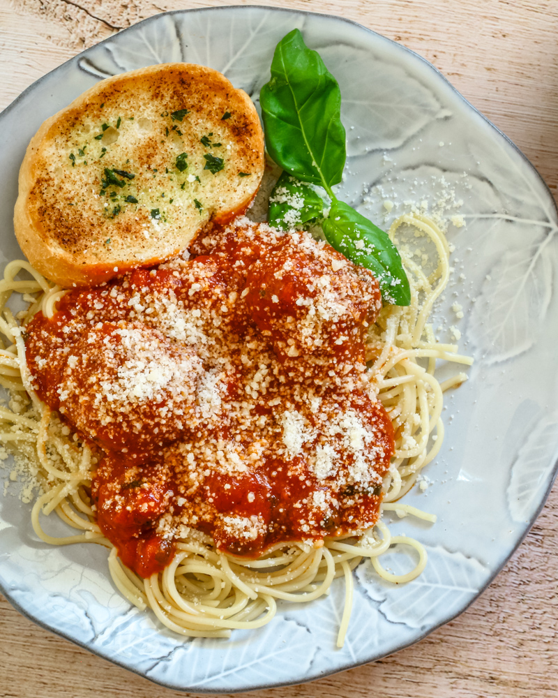 Homemade meatballs on a plate with spaghetti, garlic bread, and marinara sauce, sprinkled with Parmesan cheese.
