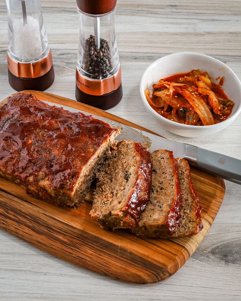Korean meatloaf on a cutting board, sliced with kimchi on the side.