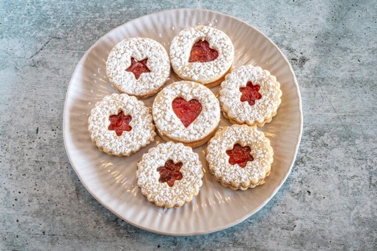 A plate of linzer cookies with jam peeking through the cutouts.