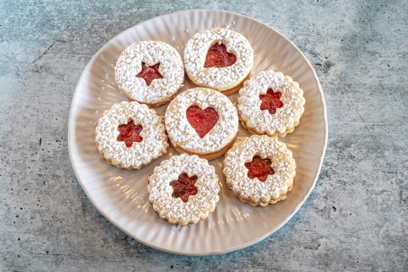 A plate of linzer cookies with jam peeking through the cutouts.