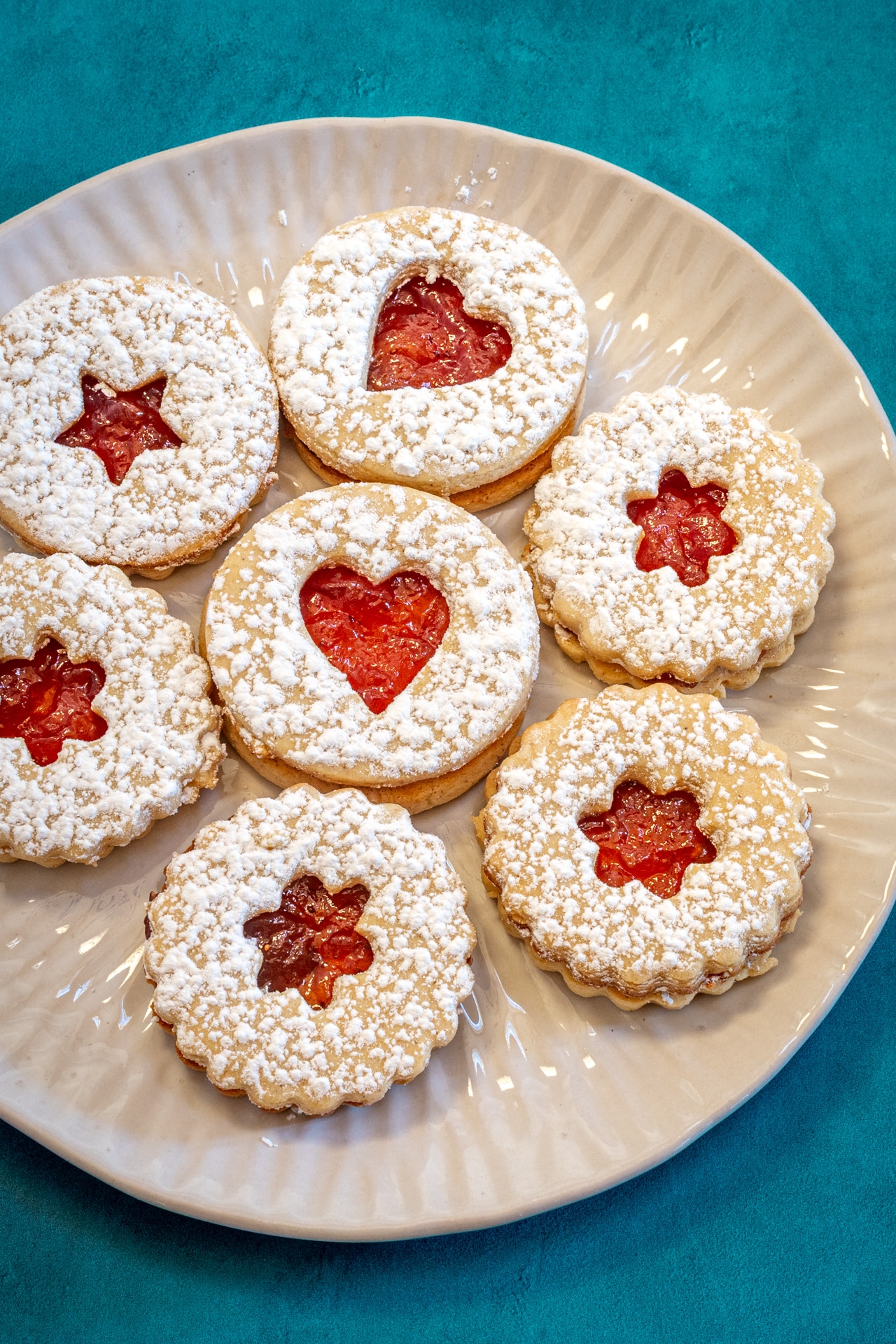 A plate of linzer cookies with jam peeking through the cutouts.