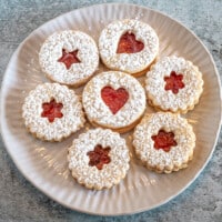 A plate of linzer cookies with jam peeking through the cutouts.