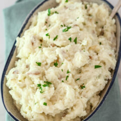 A serving bowl with make-ahead mashed potatoes, garnished with parsley.