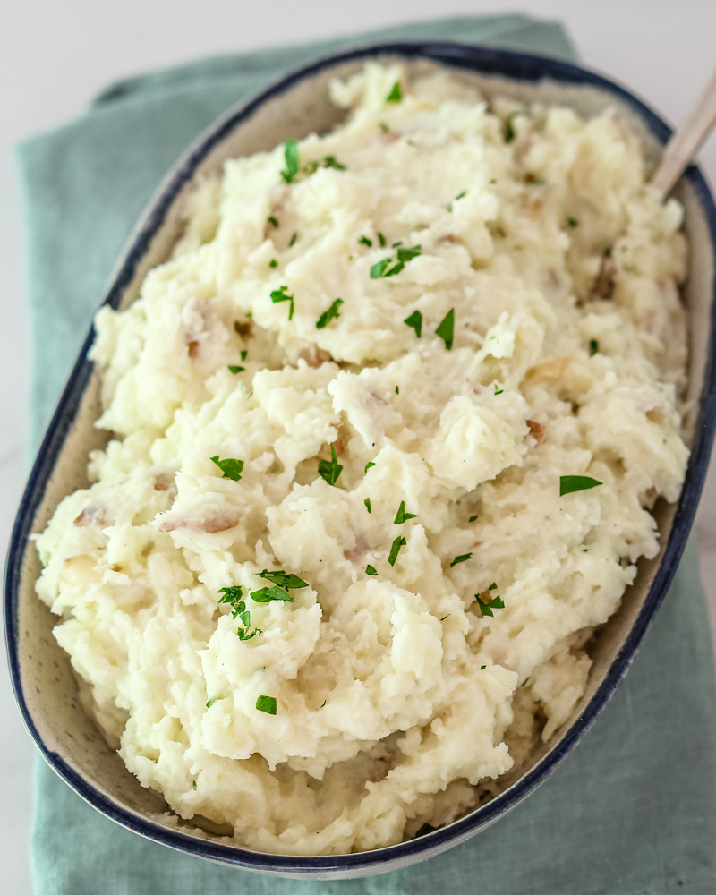 A serving bowl with make-ahead mashed potatoes, garnished with parsley.