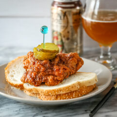 Nashville hot chicken on bred with pickles and beer in the background.