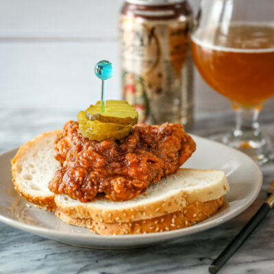 Nashville hot chicken on bred with pickles and beer in the background.