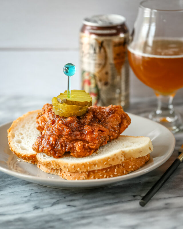 Nashville hot chicken on bred with pickles and beer in the background.