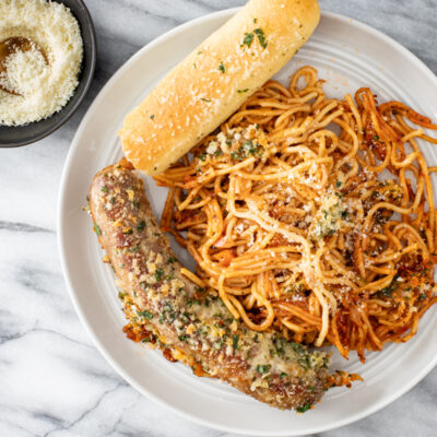 A serving of one pot spaghetti and sausages with a crispy topping and Parmesan cheese on the side.