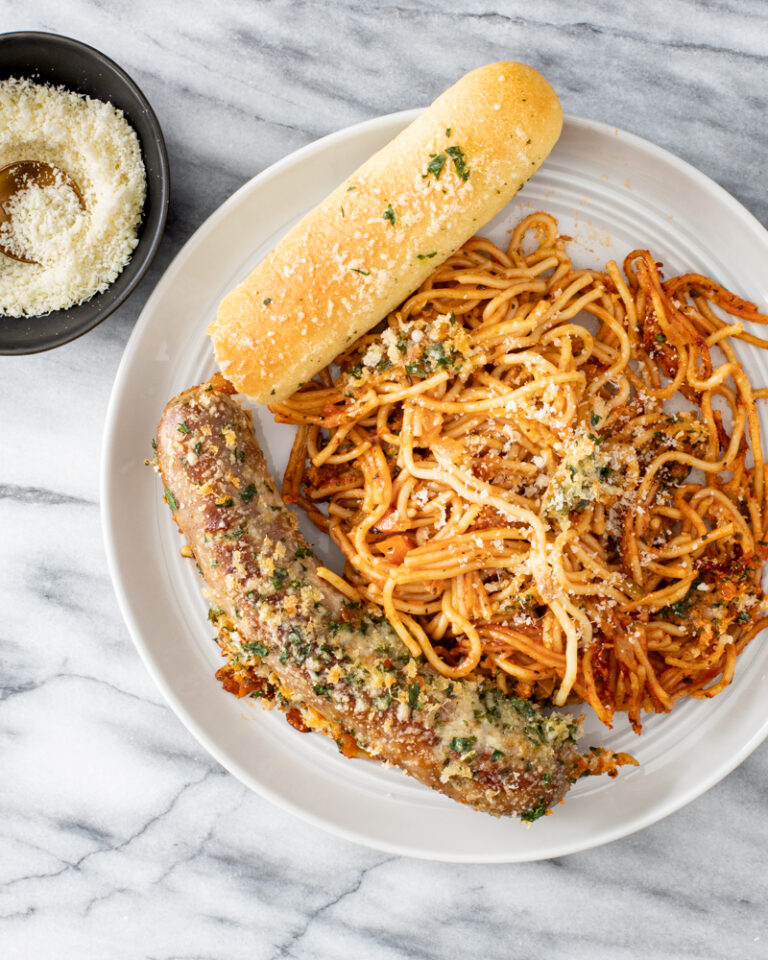 A serving of one pot spaghetti and sausages with a crispy topping and Parmesan cheese on the side.