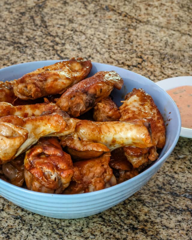 Chicken wings in a blue bowl with a small dish of dip.