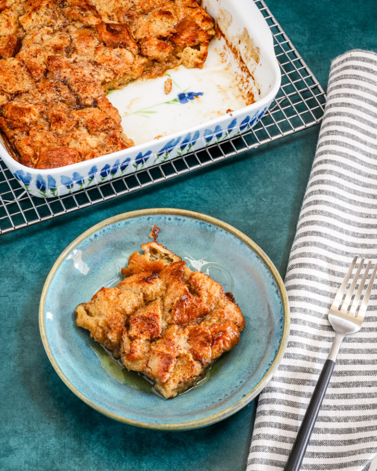 A baked French toast casserole serving with maple syrup and the casserole dish in the background.