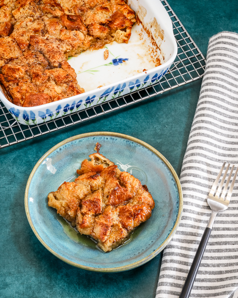 A baked French toast casserole serving with maple syrup and the casserole dish in the background.