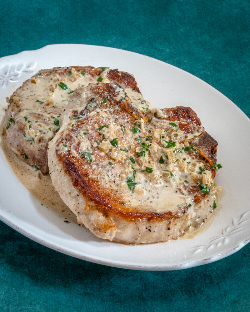 Pork chops on a plate with pan sauce drizzle.