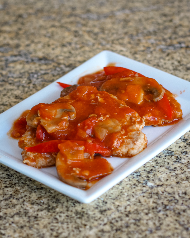pork cutlets on a serving plate with a Marengo style sauce.