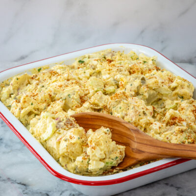 Serving potato and egg salad from a large pan with wooden spoon.