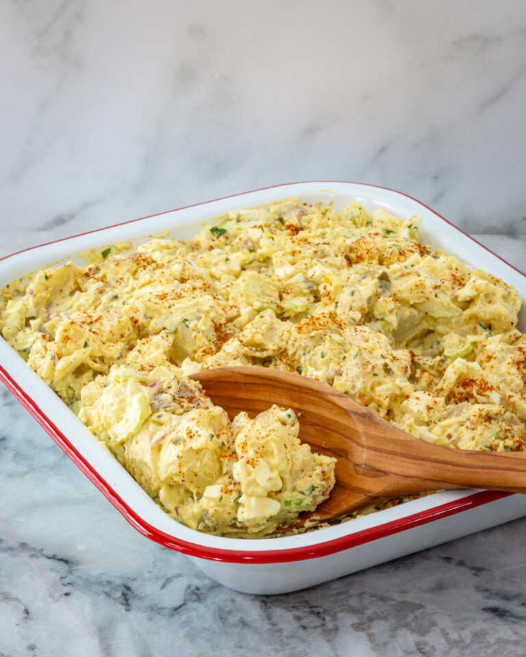 Serving potato and egg salad from a large pan with wooden spoon.