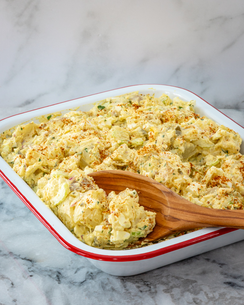 Serving potato and egg salad from a large pan with wooden spoon.
