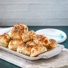 A serving tray with baked puff pastry pigs in a blanket with small appetizer plates and picks for serving.