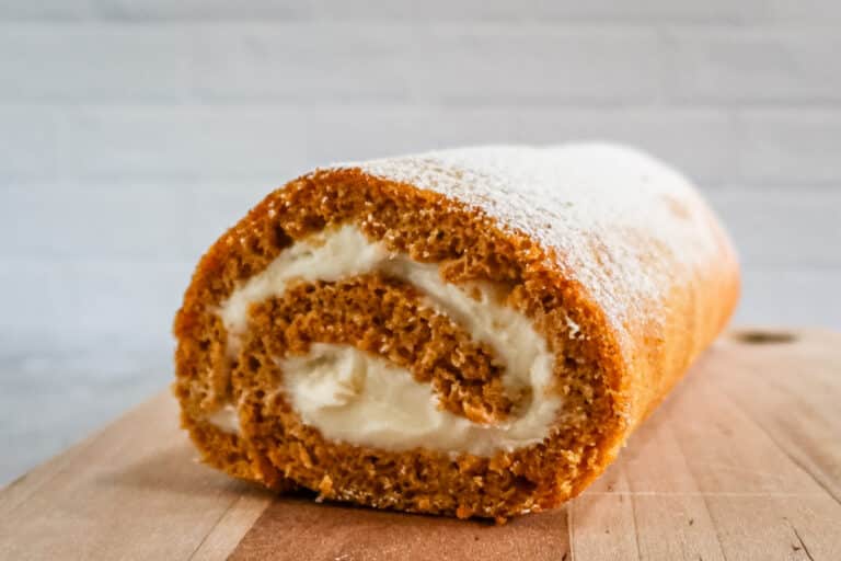 A closeup of a pumpkin roll cake with cream cheese filling, shown on a cutting board.