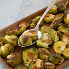 Roasted Brussels sprouts on a tray with a serving spoon.
