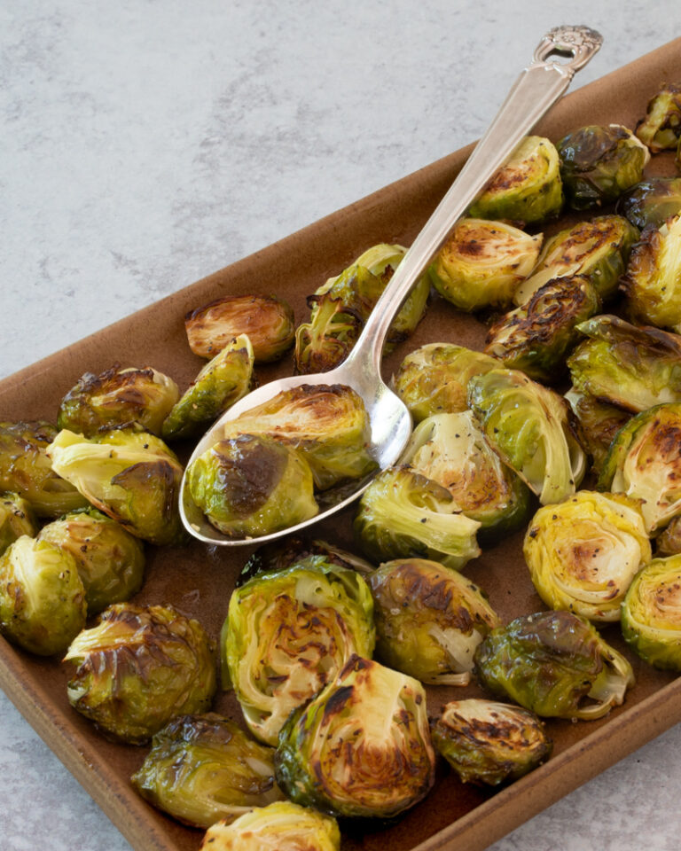 Roasted Brussels sprouts on a tray with a serving spoon.