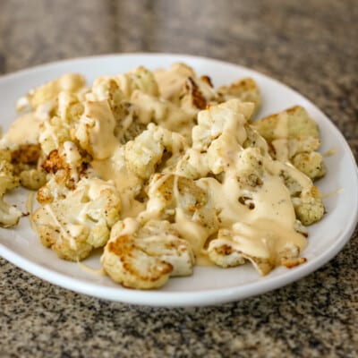 A serving plate with roasted cauliflower, topped with cheese sauce.
