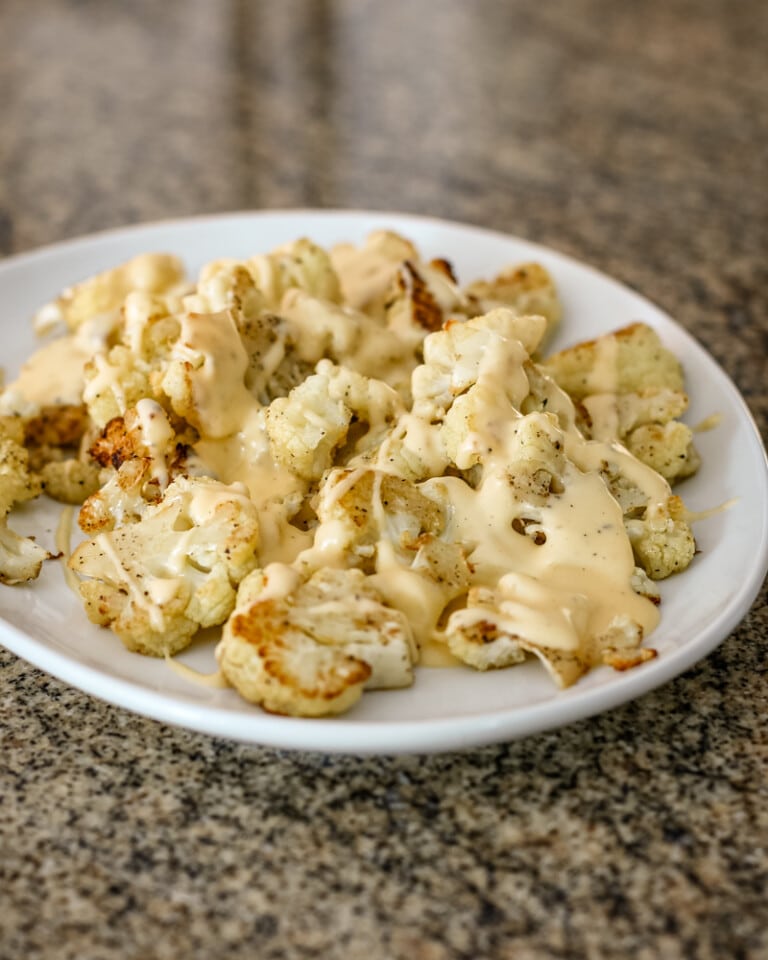 A serving plate with roasted cauliflower, topped with cheese sauce.