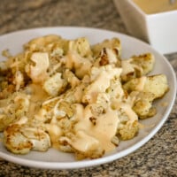 A serving plate with roasted cauliflower, topped with cheese sauce.