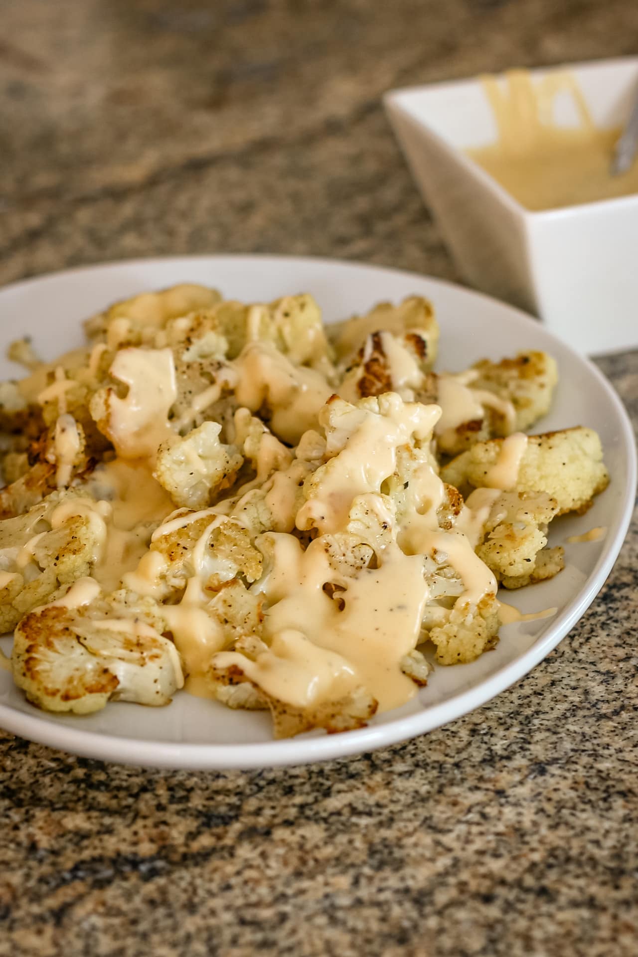A serving plate with roasted cauliflower, topped with cheese sauce.