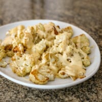 A serving plate with roasted cauliflower, topped with cheese sauce.