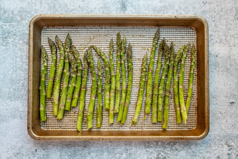 Preparing aspagagus to roast on a baking sheet with olive oil, salt, and pepper.