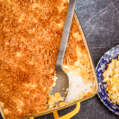 A scalloped corn casserole in a yellow baking dish with a large serving spoon.