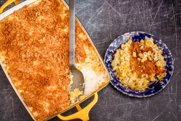 A scalloped corn casserole in a yellow baking dish with a large serving spoon.