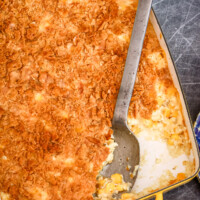 A scalloped corn casserole in a yellow baking dish with a large serving spoon.
