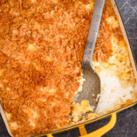A scalloped corn casserole in a yellow baking dish with a large serving spoon.