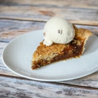 A slice of shoo fly pie on a white plate with a scoop of ice cream.
