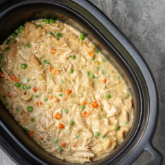 The slow cooker with finished chicken and dumplings made with refrigerated biscuits and peas and carrots.