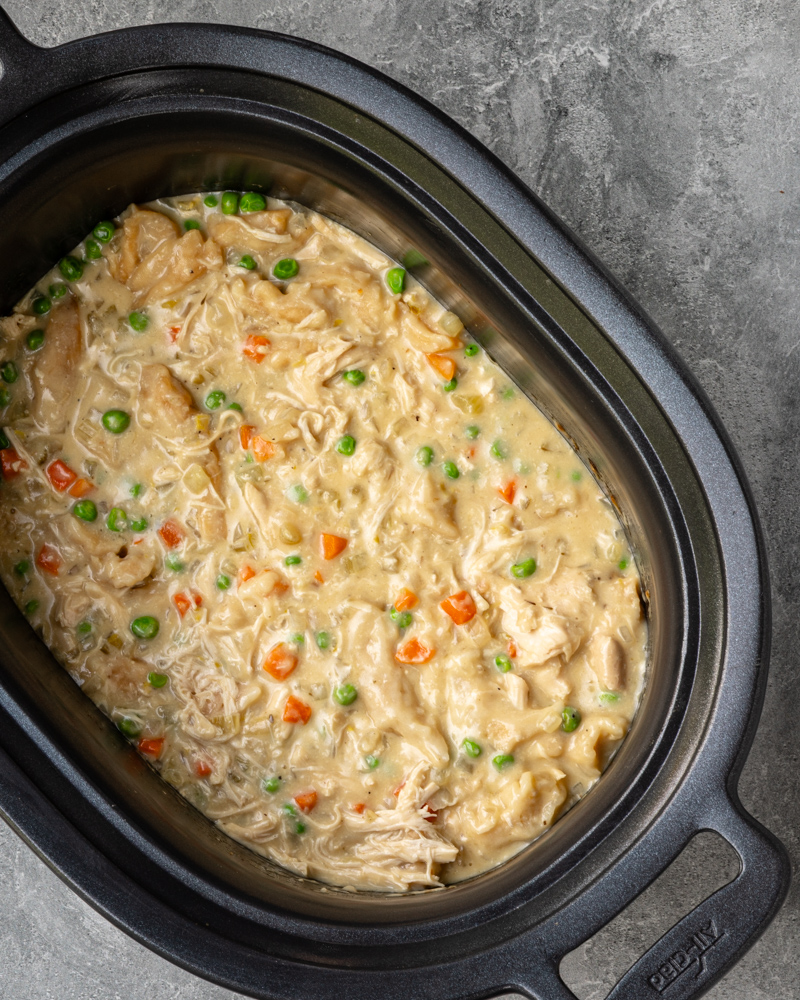 The slow cooker with finished chicken and dumplings made with refrigerated biscuits and peas and carrots.