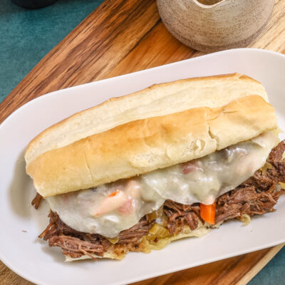 An Italian beef sandwich with cheese, on a plate.