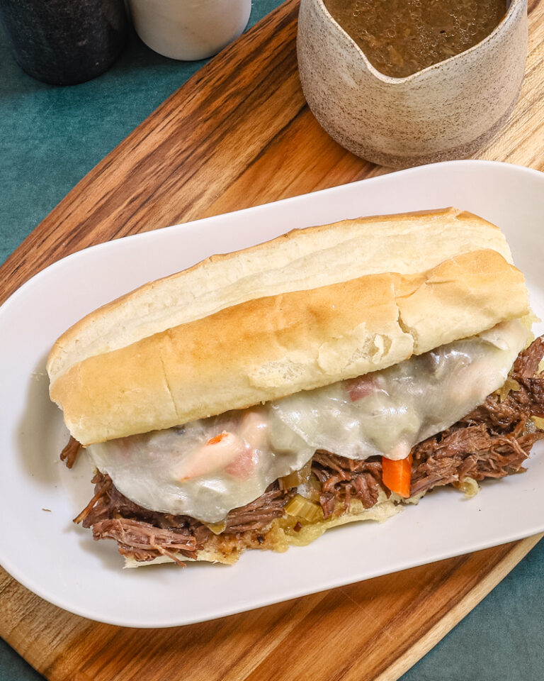 An Italian beef sandwich with cheese, on a plate.