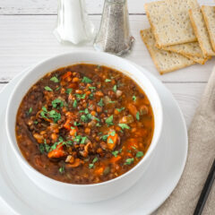 Lentil soup in a bowl with saltine crackers and salt and pepper shakers in the background.