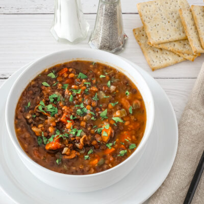 Lentil soup in a bowl with saltine crackers and salt and pepper shakers in the background.