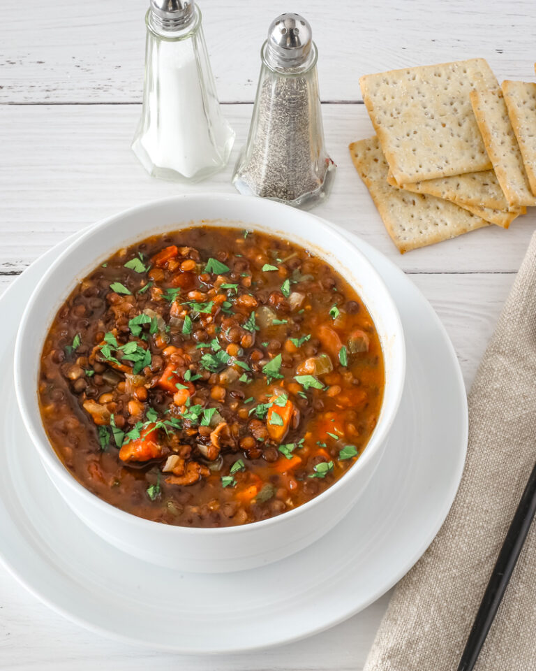 Lentil soup in a bowl with saltine crackers and salt and pepper shakers in the background.
