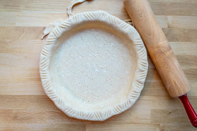 An unbaked pie shell with fork-fluted edges and a rolling pin beside it.