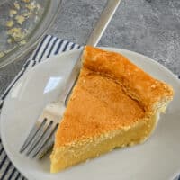A white plate with a slice of chess pie, on a striped cloth with a fork.