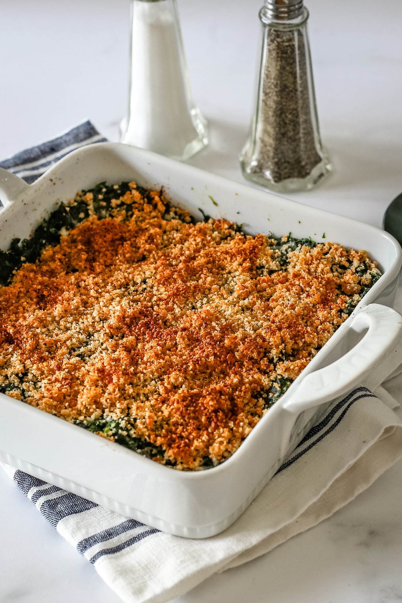 A spinach casserole in a baking dish with crumb topping.